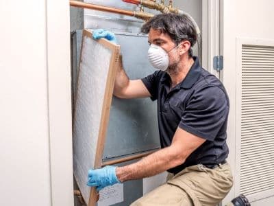 A man wearing gloves and a mask is working on an air conditioner.