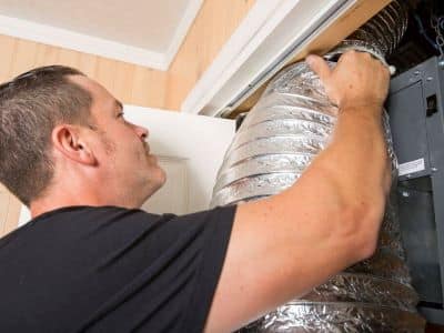 A man is working on the outside of an air vent.